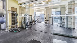 A modern gym with various exercise equipment, large windows, and a city view.