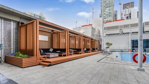 A rooftop terrace with wooden seating, a pool, and a view of the city skyline.
