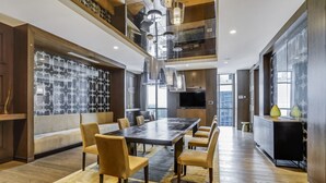 A modern dining area with a large table and chairs, a kitchen with a TV, and a decorative wall with a pattern.
