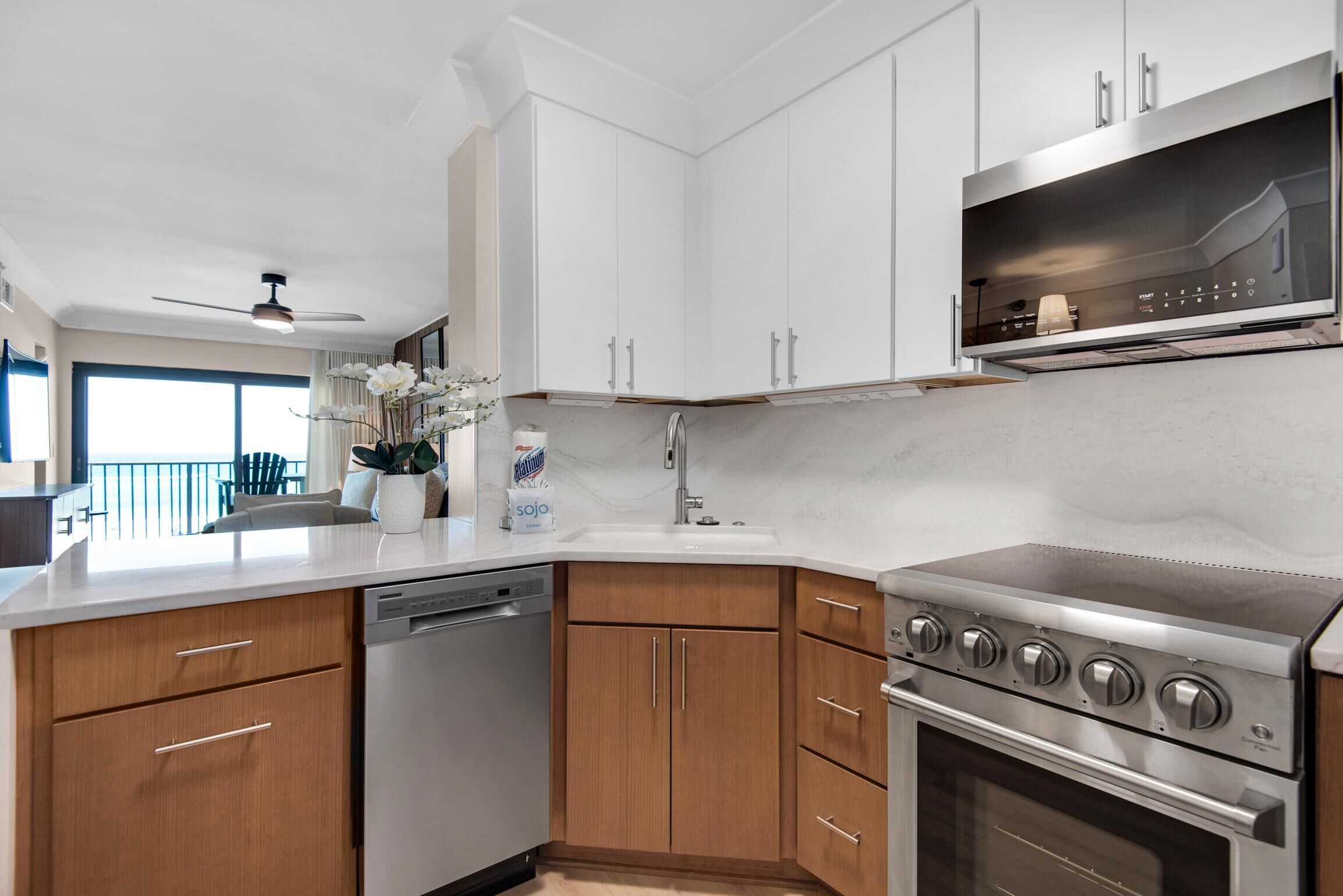 A modern kitchen with white cabinets, a dishwasher, a stove, and a large window.