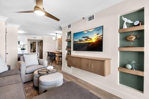 A modern living room with a ceiling fan, a flat-screen TV, and a dining area in the background.