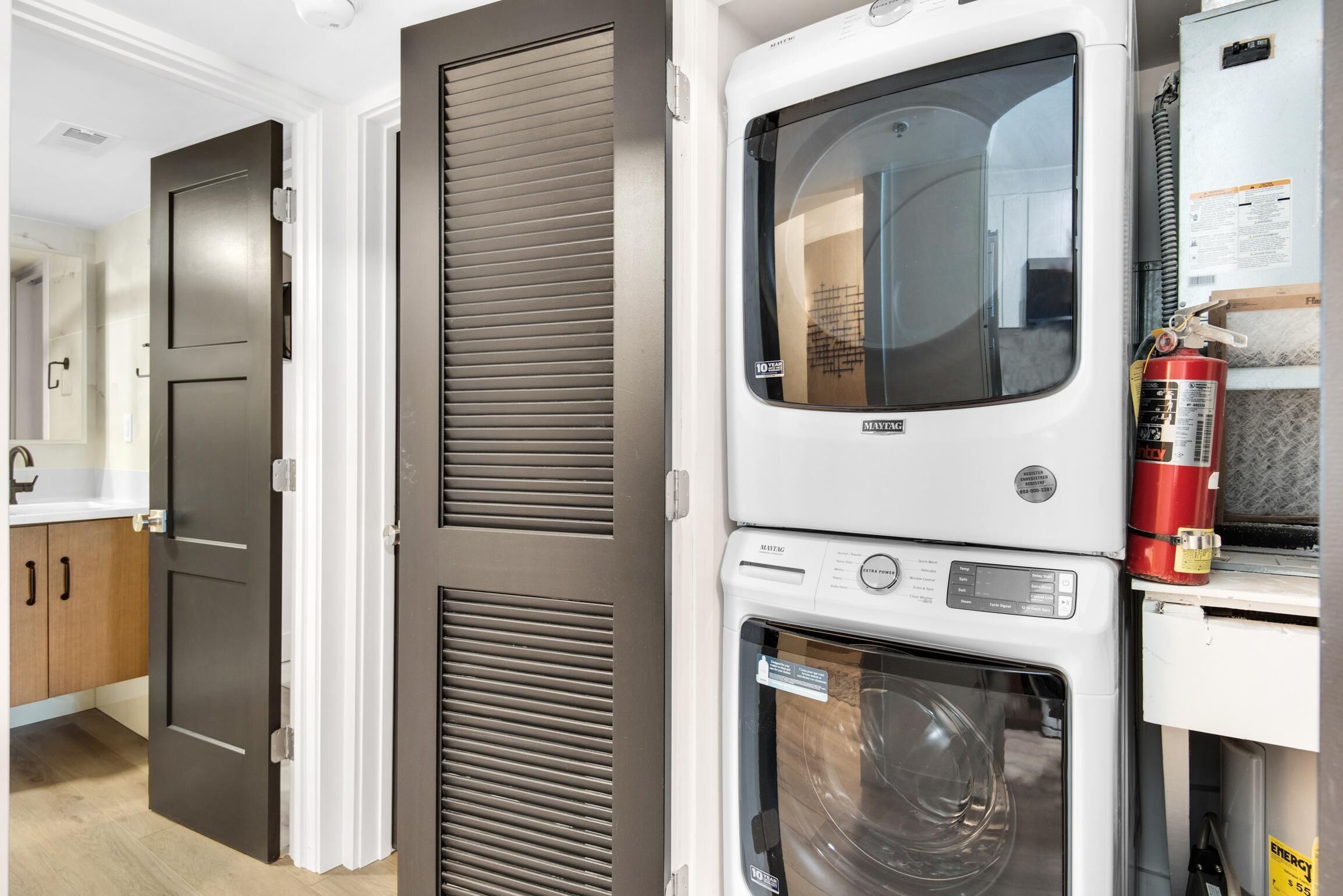 A compact laundry area with a washing machine, dryer, and a fire extinguisher.