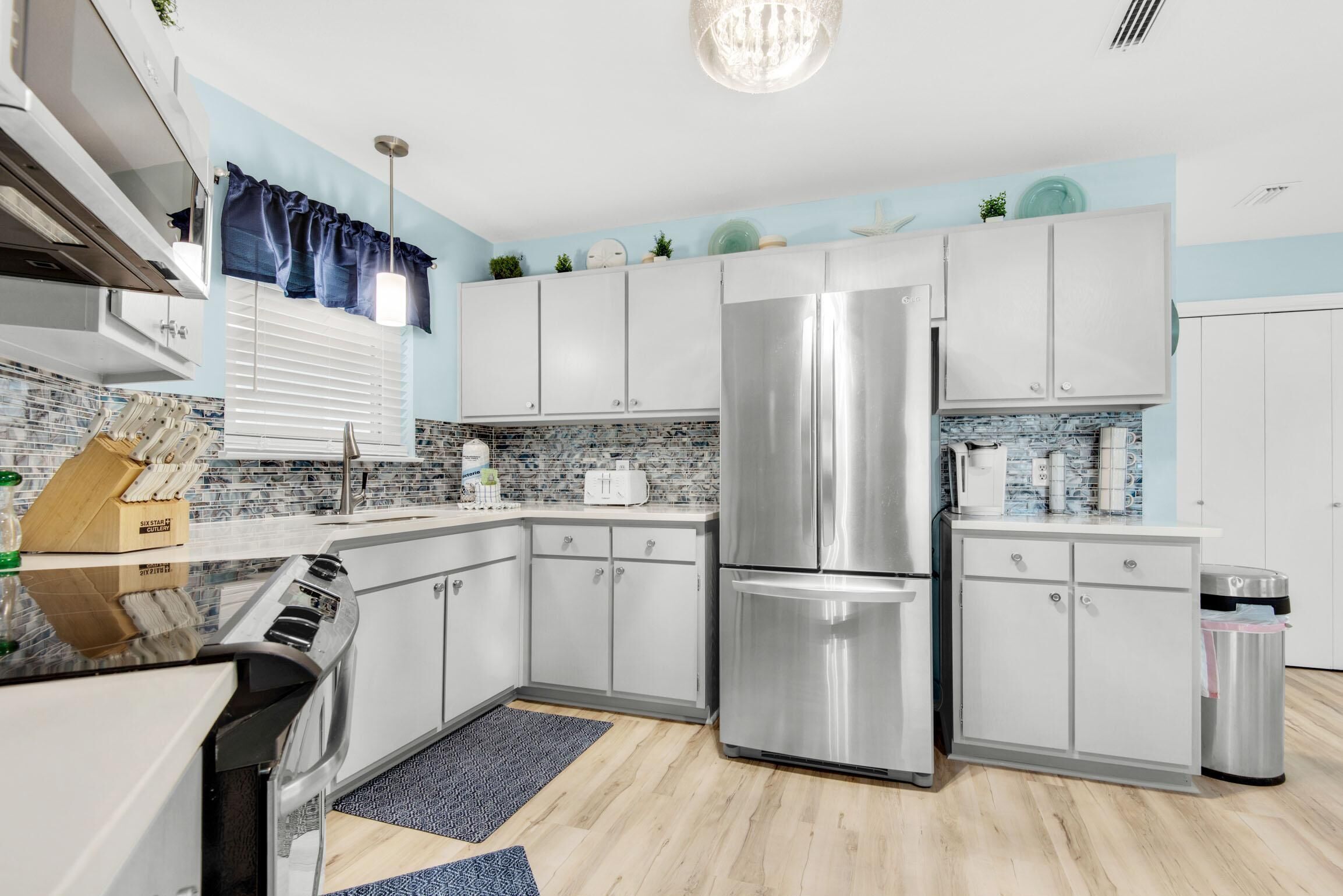 A modern kitchen with white cabinets, a stainless steel refrigerator, and a blue and white backsplash.