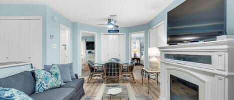 A living room with a sofa, coffee table, fireplace, TV, and a dining area with chairs.