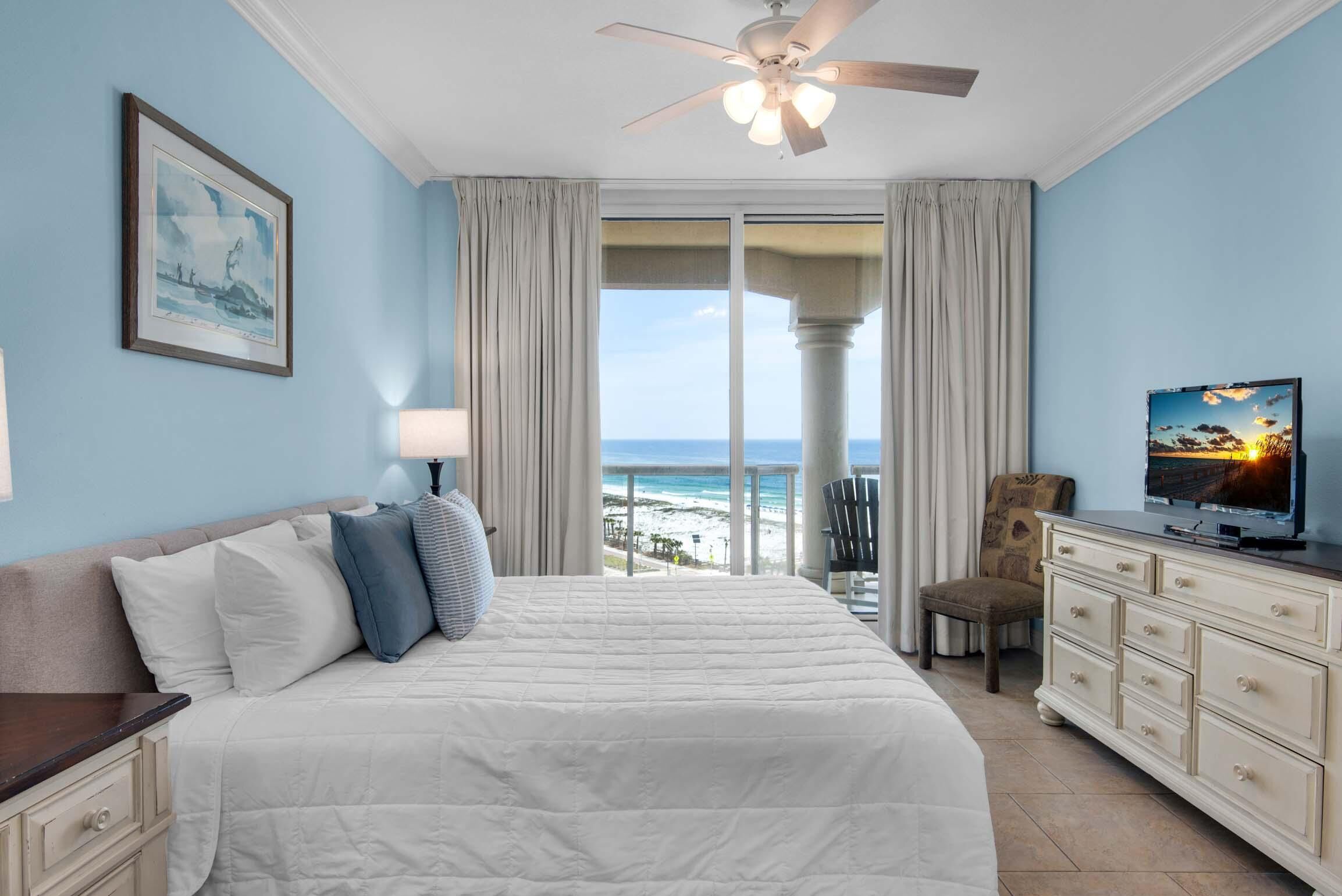 A bedroom with a bed, a television, a dresser, and a view of the beach.