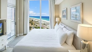 A hotel room with a large bed, a ceiling fan, a TV, and a view of the beach and cityscape. - Portofino Island Resort 1- 809 (Pensacola Beach)