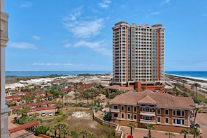 A high-rise hotel with multiple balconies, a beach view, and a parking area with a few cars. - Portofino Island Resort 1- 809 (Pensacola Beach)