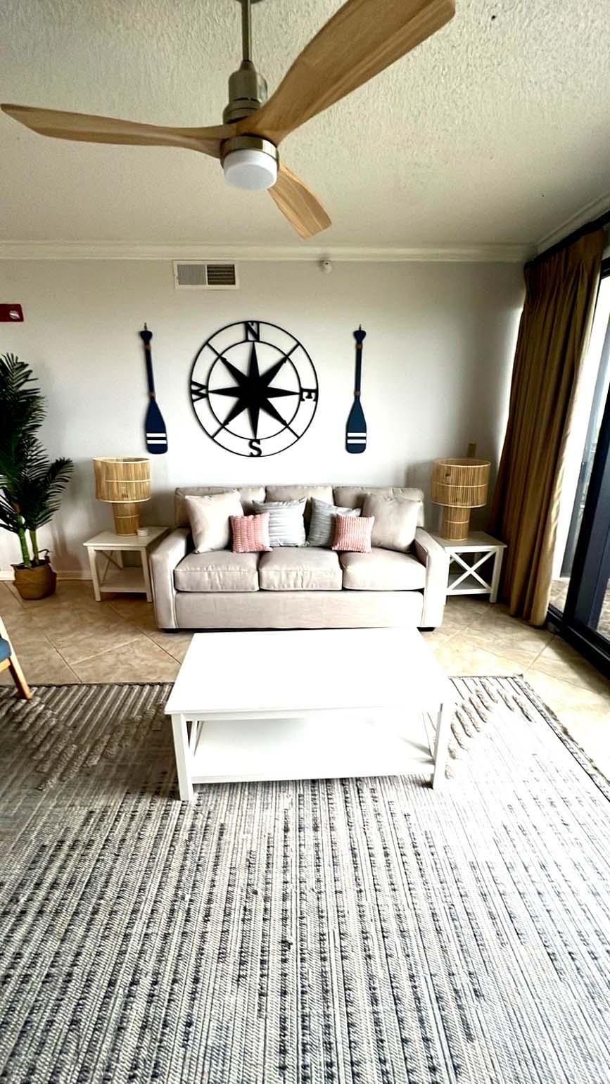 A living room with a ceiling fan, a compass wall decoration, a sofa, and a coffee table.