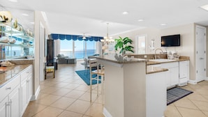 A modern kitchen with a central island, a dining area with a view, and a living room with a large window. - Belle Mer 1102 (Navarre)