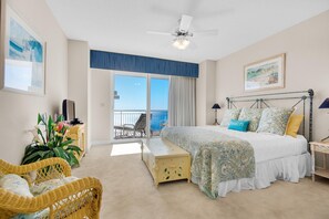 A bedroom with a bed, a chair, a bedside table, a ceiling fan, and a balcony with a view. - Belle Mer 1102 (Navarre)