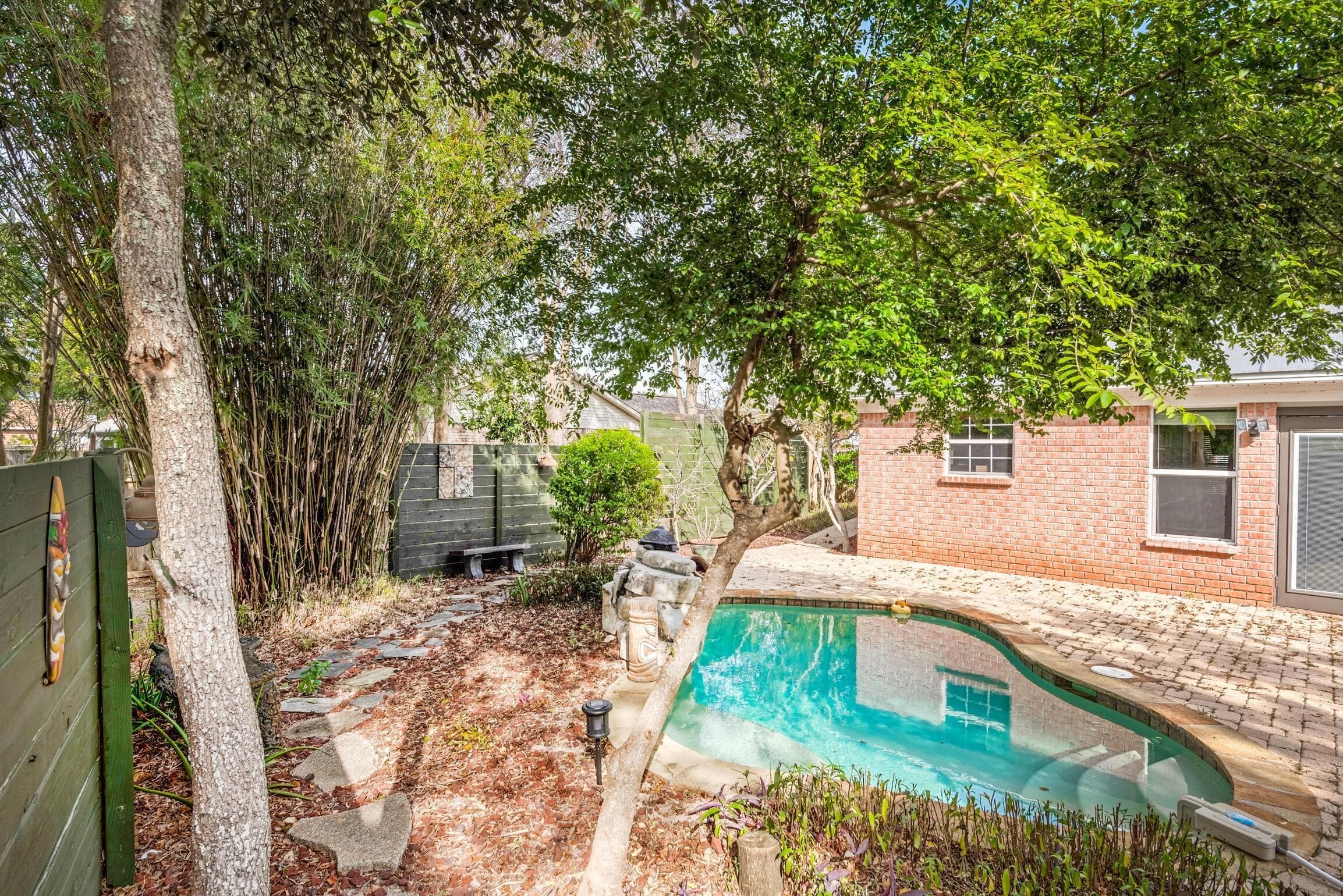 Un patio trasero con una piscina, una casa de ladrillo y un árbol.
