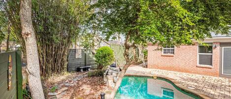 Un patio trasero con una piscina, una casa de ladrillo y un árbol.
