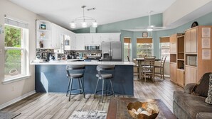 A modern kitchen with a central island, bar stools, and wooden cabinets. - Village Oasis (Gulf Breeze)