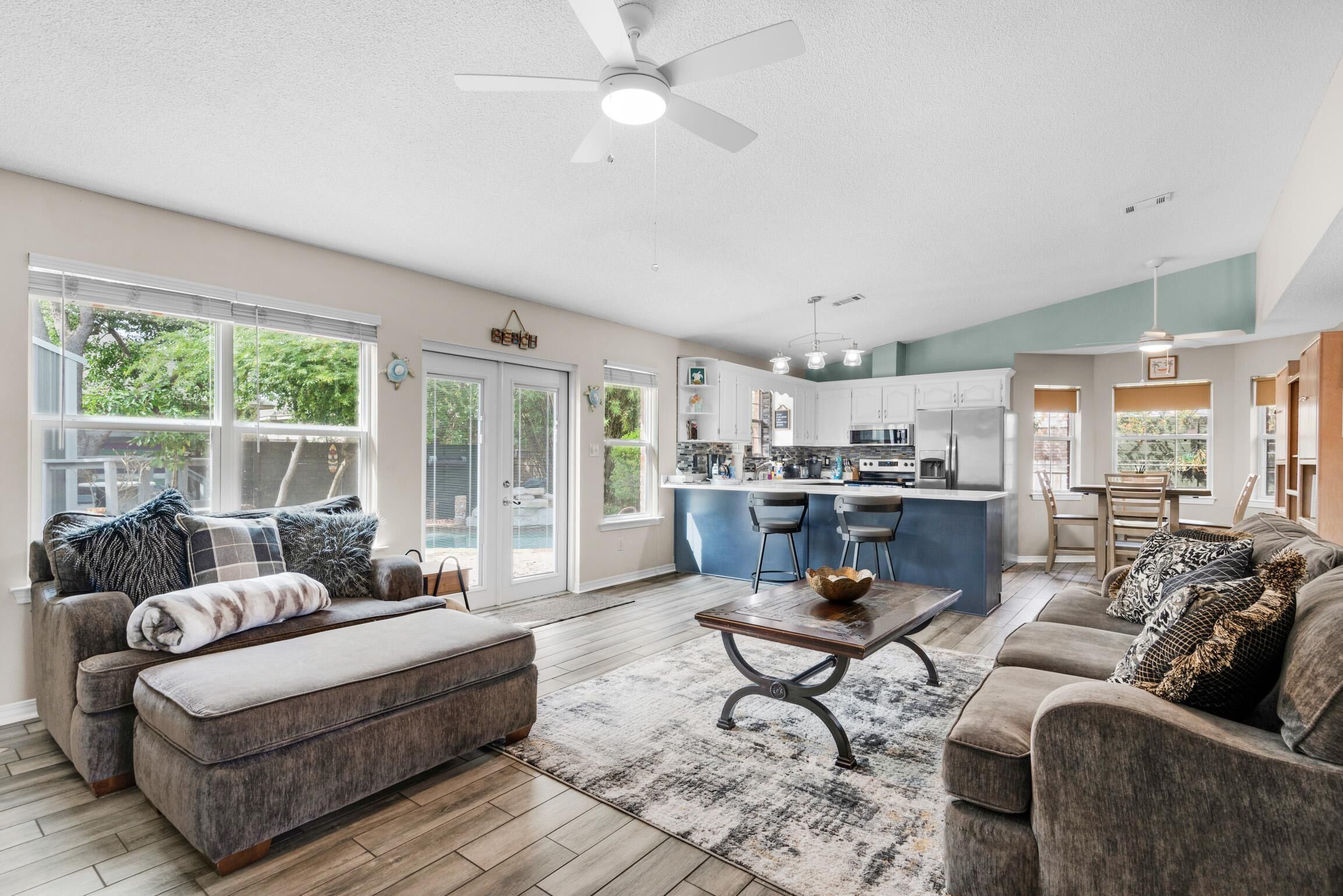 A spacious living room with a large window, a ceiling fan, and a kitchen area with bar stools.