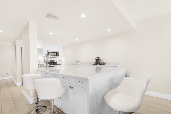 A modern kitchen with white cabinetry, a marble countertop, and two bar stools.