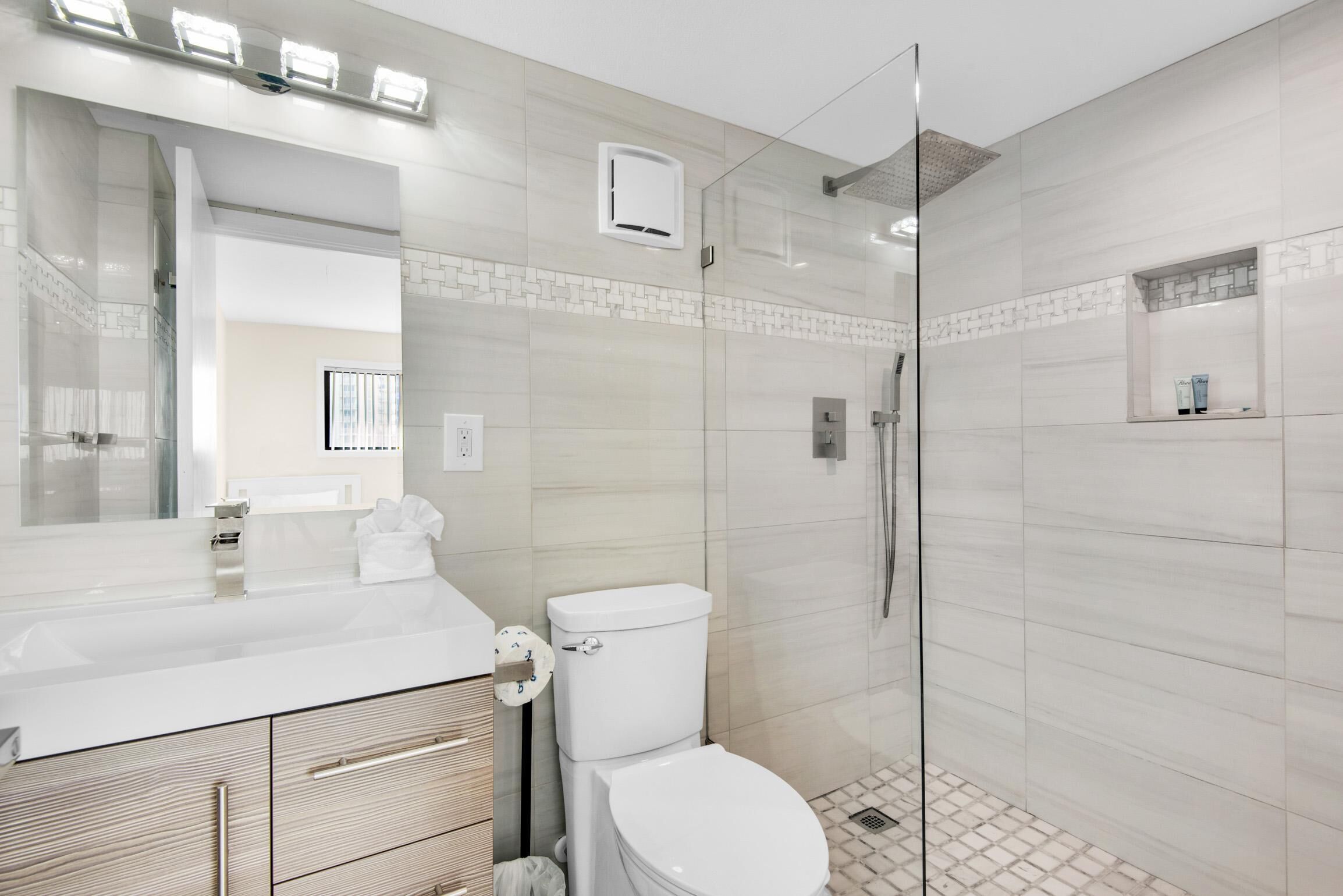 Et moderne badeværelse med et hvidt toiletbord, toilet og en brusekabine i glas.
