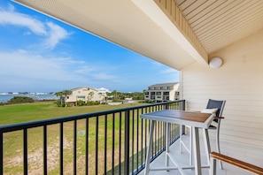 A balcony with a table and chairs, overlooking a grassy area and buildings. - Santa Rosa Dunes 425 (Pensacola Beach)