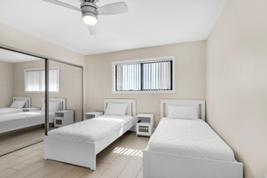 Un dormitorio moderno con dos camas individuales, un ventilador de techo, una ventana con persianas y un espejo en la pared.