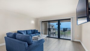 Ein modernes Wohnzimmer mit einem blauen Sofa, einem weißen Couchtisch und einem großen Fernseher.