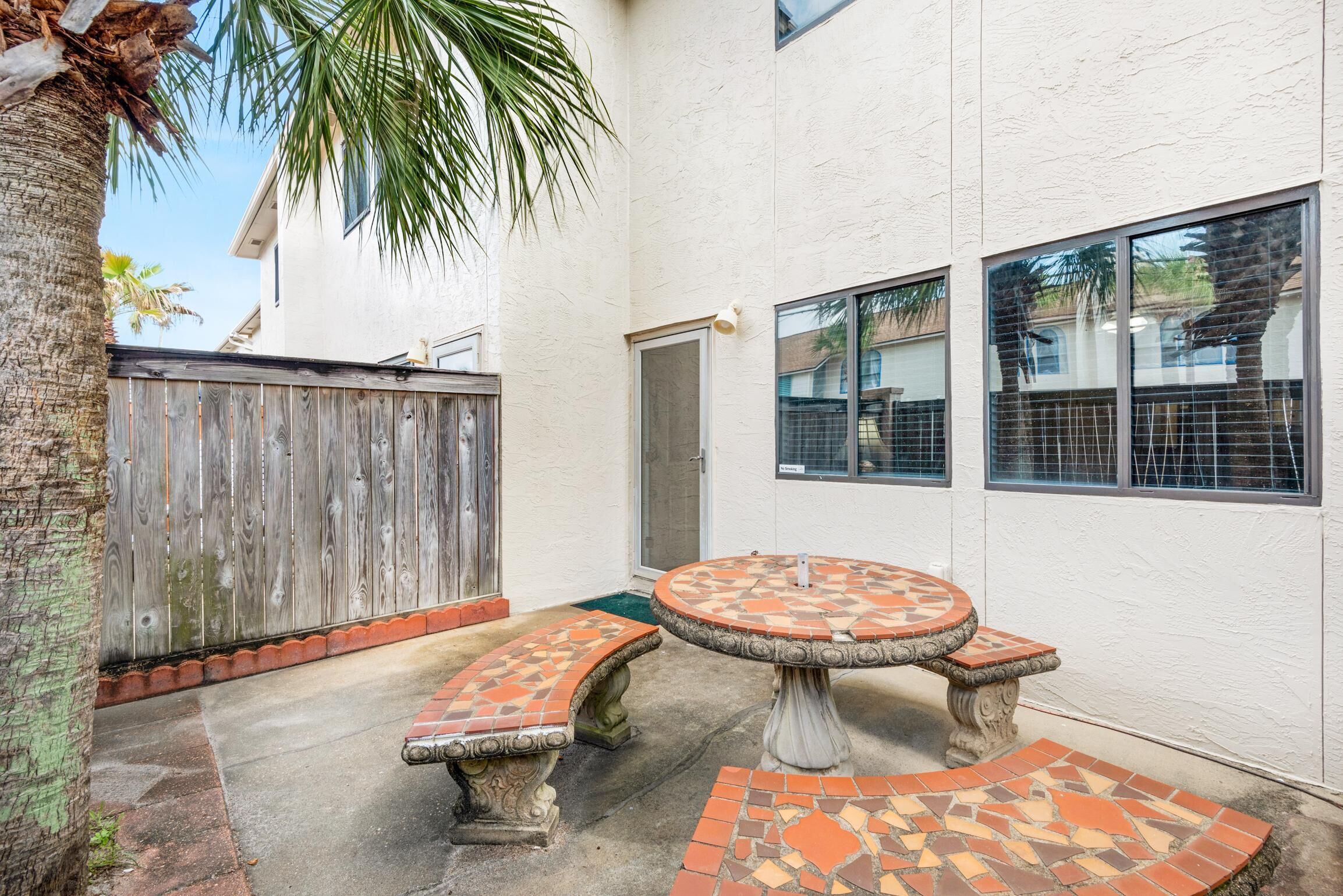 Une terrasse avec une table ronde et des bancs, une clôture en bois et un bâtiment doté de fenêtres.