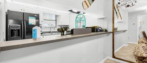 A kitchen with a refrigerator, a coffee machine, and a sink. There are wooden paddles hanging on the wall and a motivational quote.