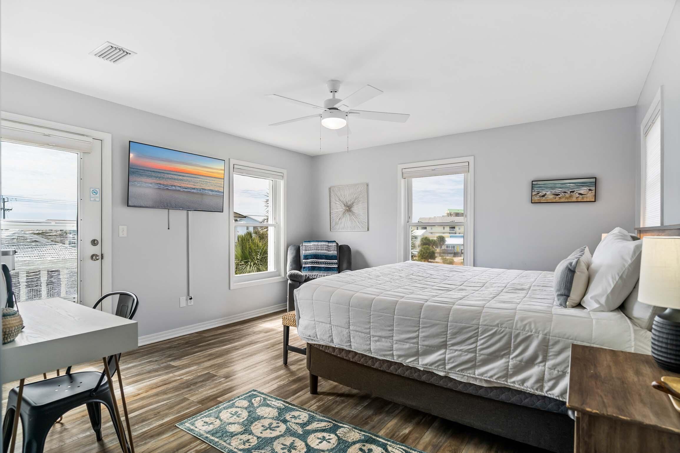 A bedroom with a bed, a desk, and a chair. There is a window with a view of the city.