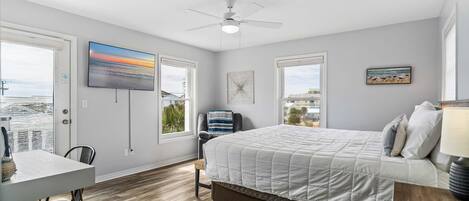 A bedroom with a bed, a desk, and a chair. There is a window with a view of the city.