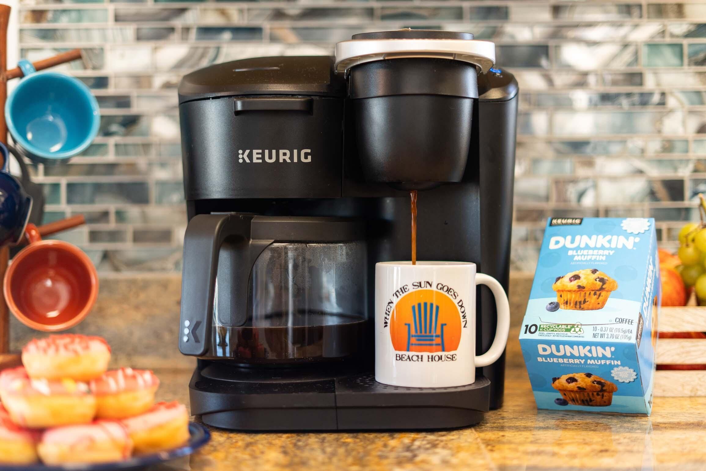 A Keurig coffee maker with a mug labeled "When the sun goes down, Beach House" and a box of Dunkin' Blueberry Muffin coffee.