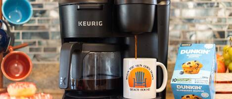 A Keurig coffee maker with a mug labeled "When the sun goes down, Beach House" and a box of Dunkin' Blueberry Muffin coffee.
