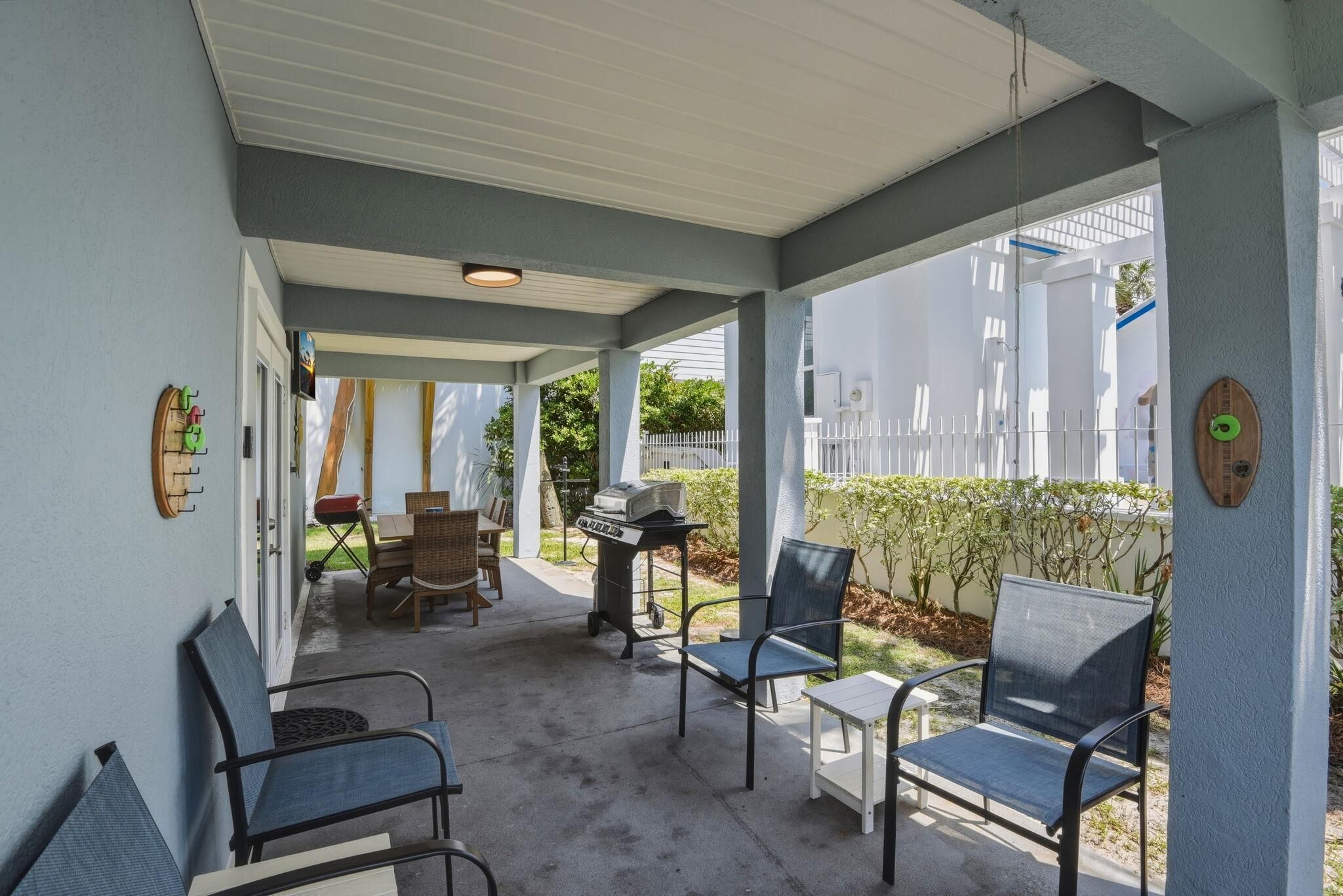 A covered outdoor seating area with chairs and a table, a barbecue grill, and a wall-mounted clock.