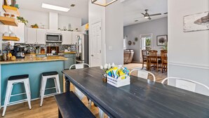 Eine moderne Küche mit weißen Schränken, einer schwarzen Arbeitsplatte und einem Essbereich mit einem dunklen Holztisch und weißen Stühlen.