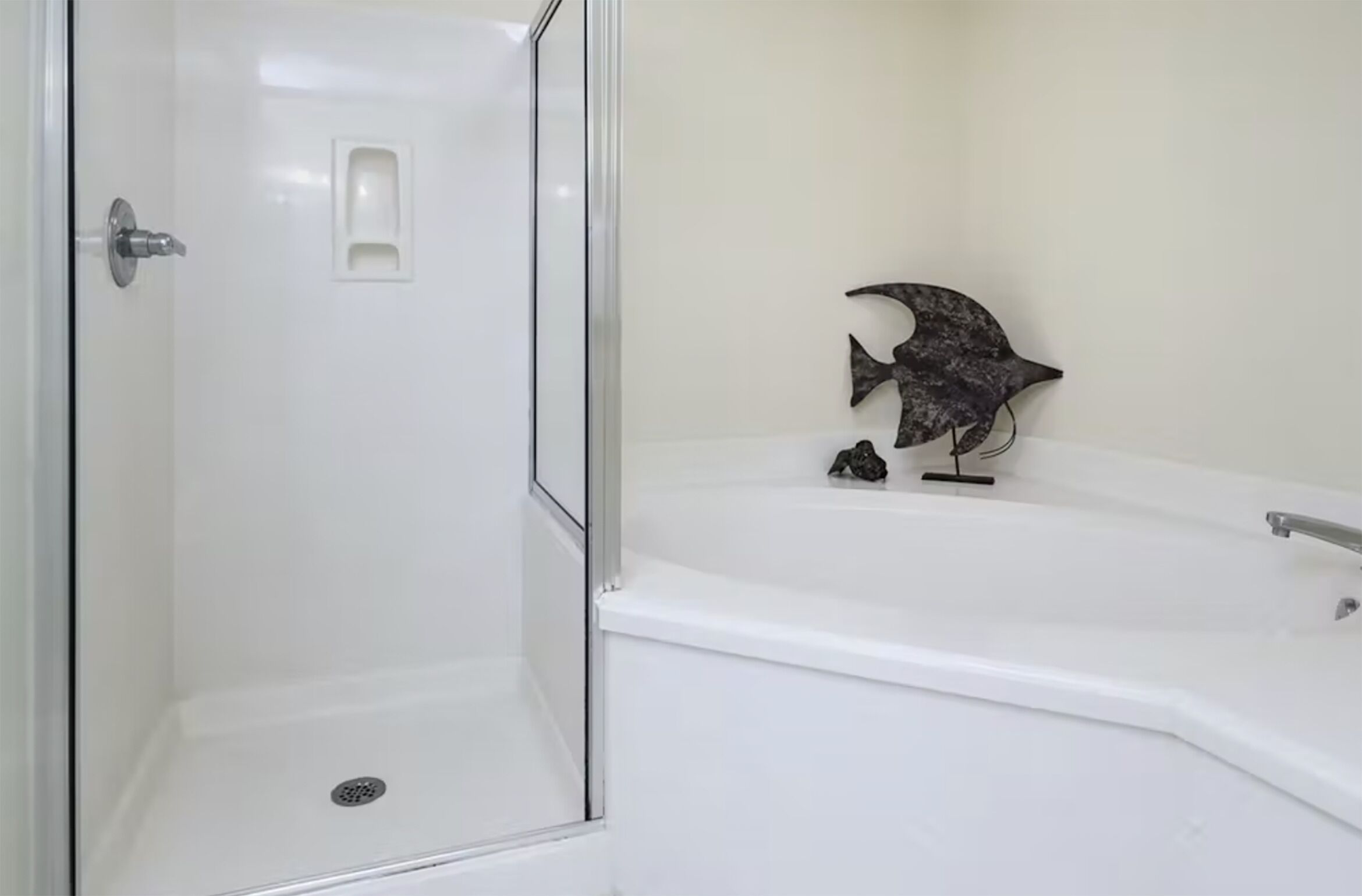 A bathroom with a glass-enclosed shower, a white bathtub, and a small decorative fish sculpture.