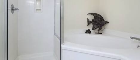 A bathroom with a glass-enclosed shower, a white bathtub, and a small decorative fish sculpture.