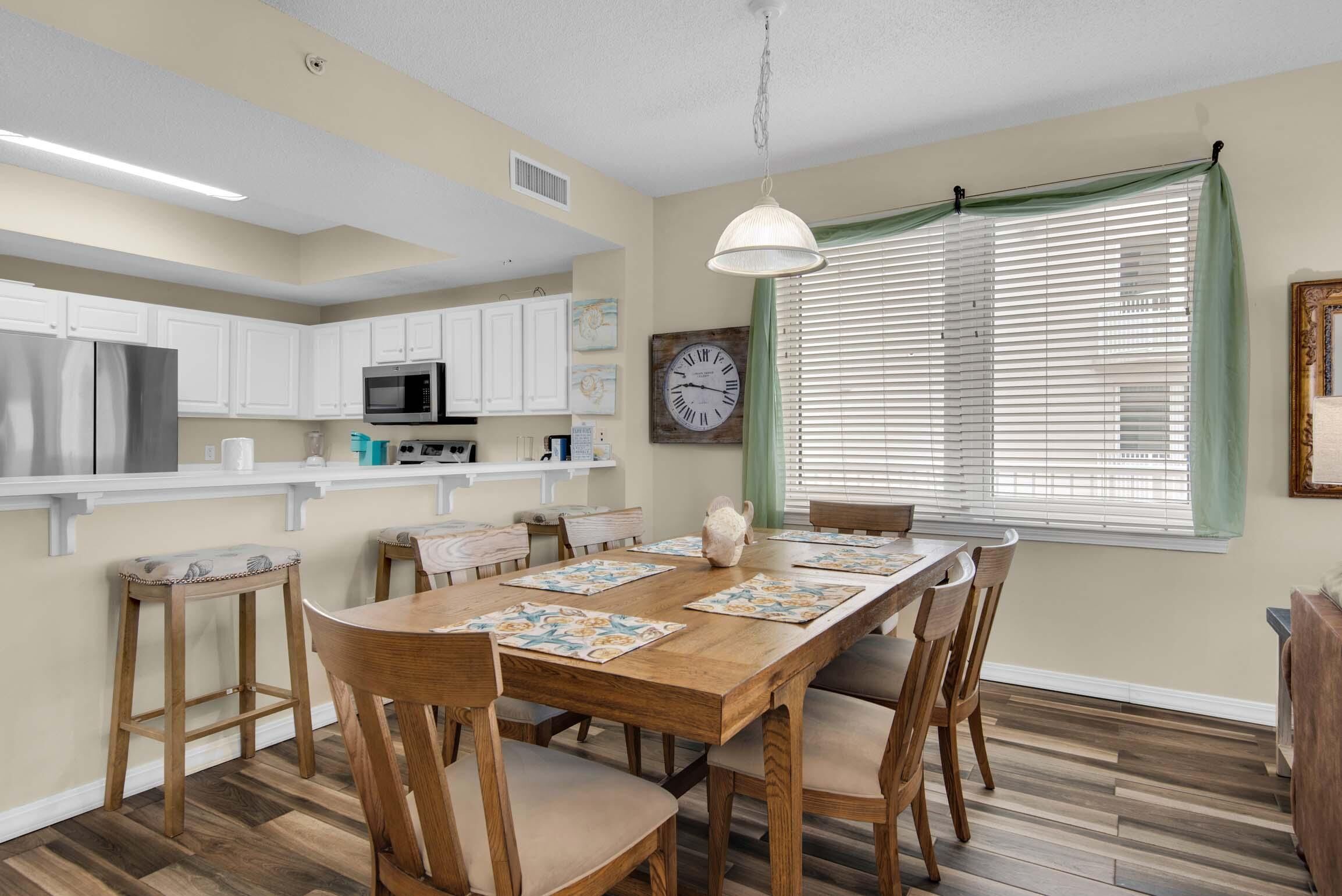 A dining area with a wooden table, chairs, a clock, and a window with blinds.
