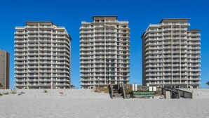 Tres edificios altos con balcones, una playa arenosa y una escalera que lleva a la playa.