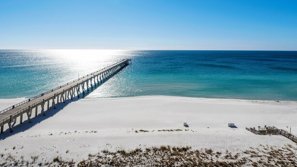 A beach with a pier extending into the ocean, a sandy shore, and clear skies. - Summerwind Center 704 (Navarre)