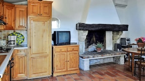 Cocina rústica con armarios de madera, chimenea de piedra y comedor con mesa y sillas.