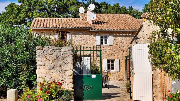 Una casa de piedra con techo de tejas, antenas parabólicas, un portón verde y una puerta blanca.