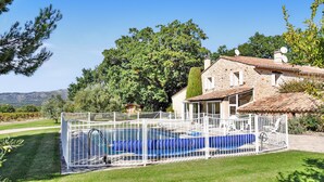 Una casa de piedra con piscina rodeada por una cerca blanca.