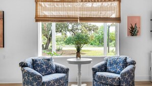 Ein Zimmer mit zwei blauen Sesseln, einem kleinen weißen Tisch, einem Fenster mit Blick auf Grünflächen und einem an der Wand befestigten Schild mit der Aufschrift 'Beach'.