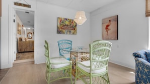 A dining area with wicker chairs, a glass table, and a hanging light fixture. - Bungalow By the Sea-mermaid (Navarre)