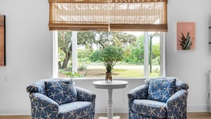 A room with two blue armchairs, a small white table, a window with a view of greenery, and a wall-mounted sign reading 'Beach'. - Bungalow By the Sea-mermaid (Navarre)