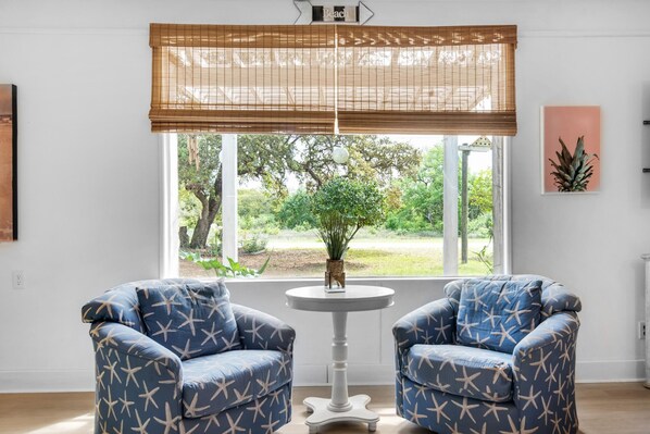 Una habitación con dos sillones azules, una mesita blanca, una ventana con vistas a zonas verdes y un letrero en la pared que dice 'Beach'.