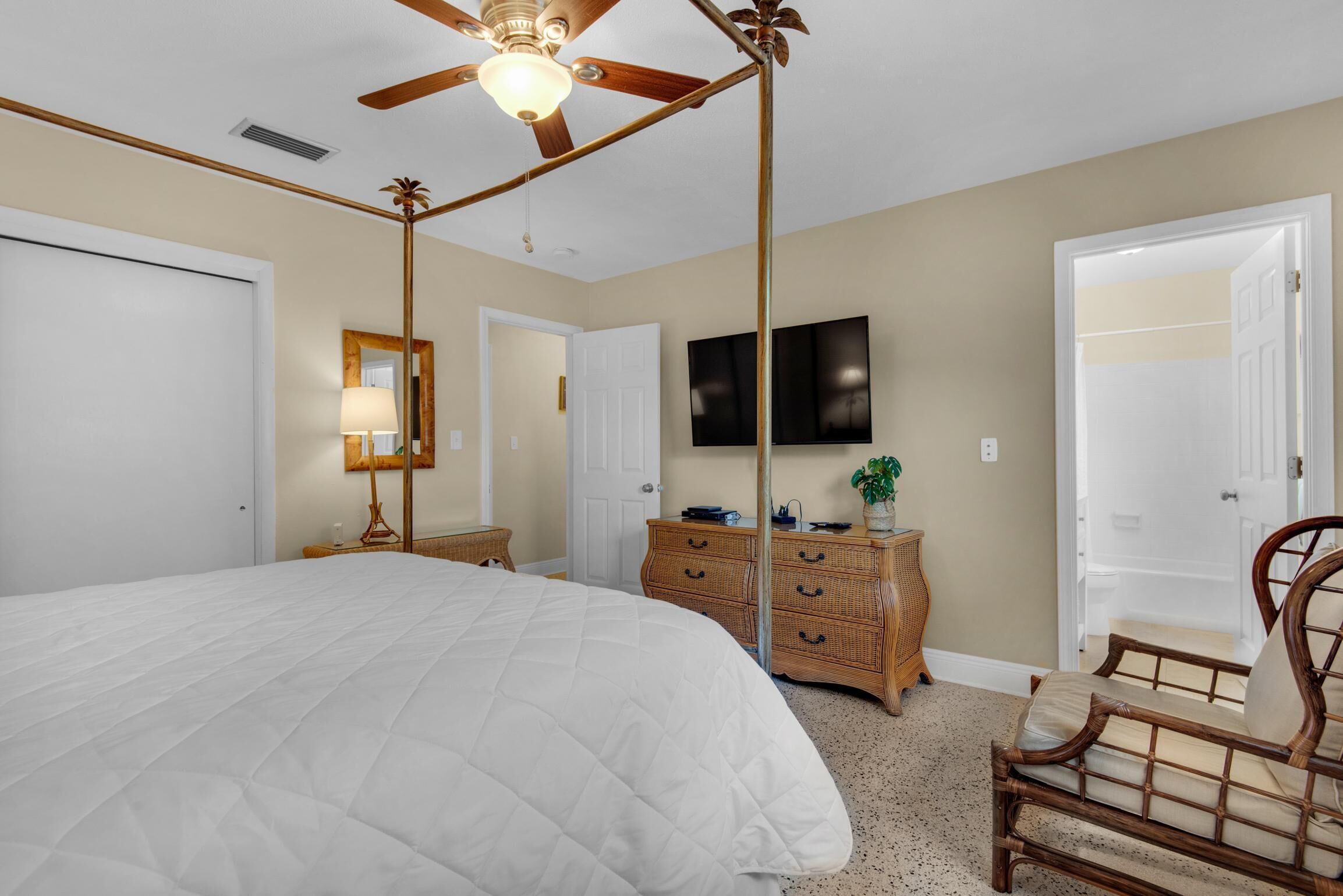 A bedroom with a large bed, a ceiling fan, a dresser, a chair, and a television on the wall.