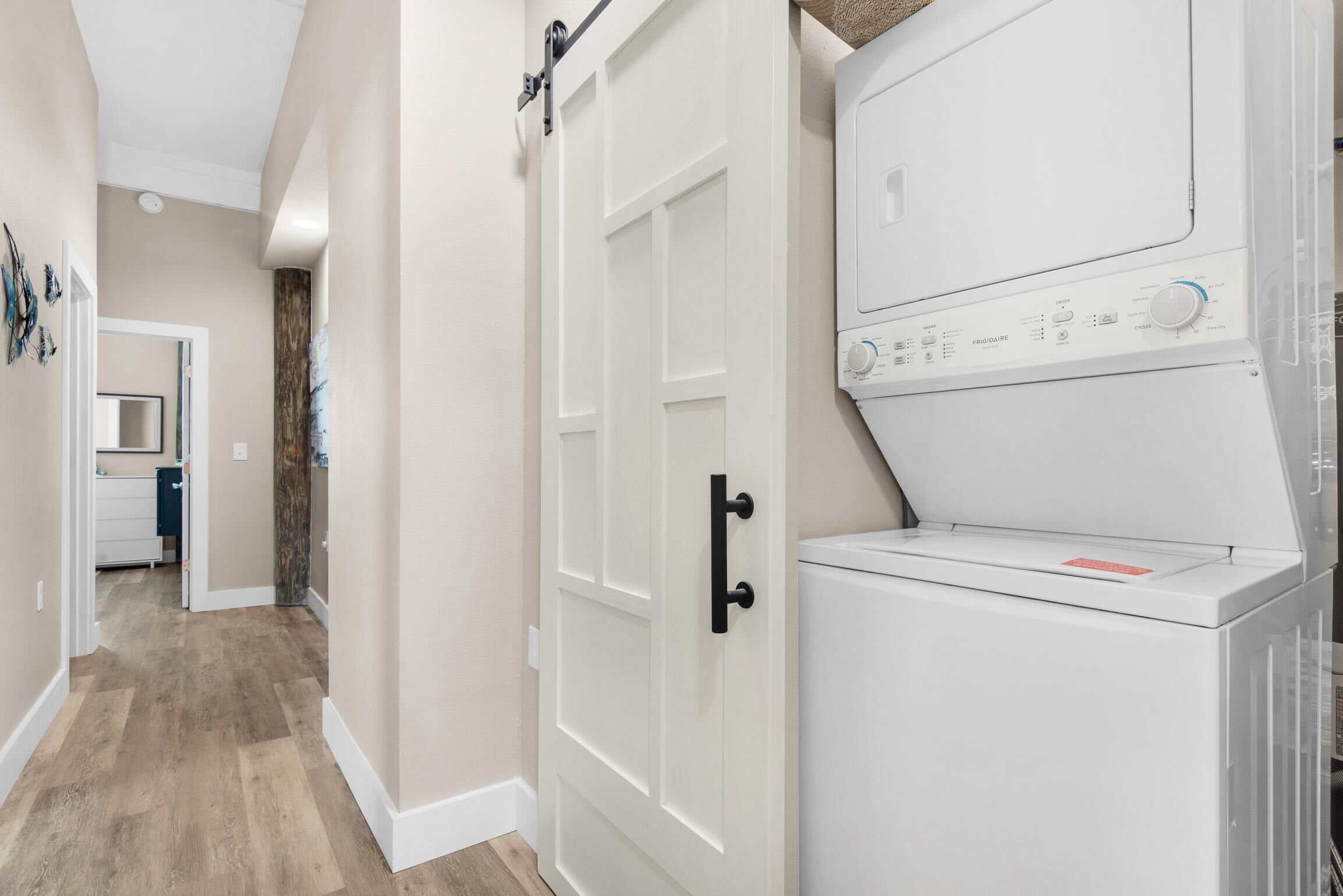 A laundry room with a white washer and dryer, a wooden floor, and a door with a black handle.