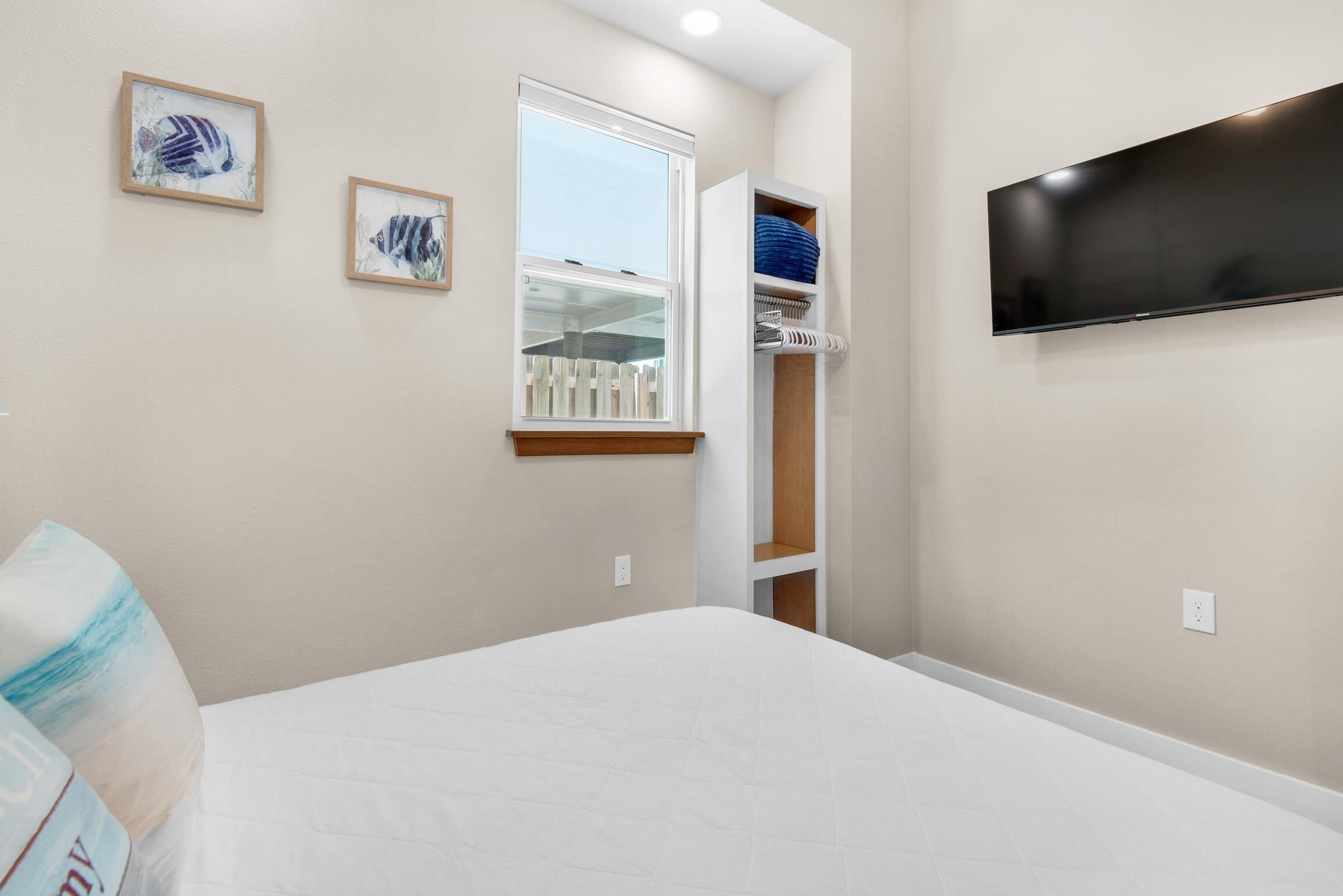 Un dormitorio con una cama, una ventana, un televisor montado en la pared y un armario con estantes.