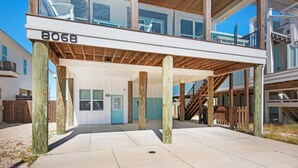 A beachfront property with a covered outdoor area supported by wooden posts, a visible door, and a staircase leading to an upper level. - Para-dise LZ (Navarre)