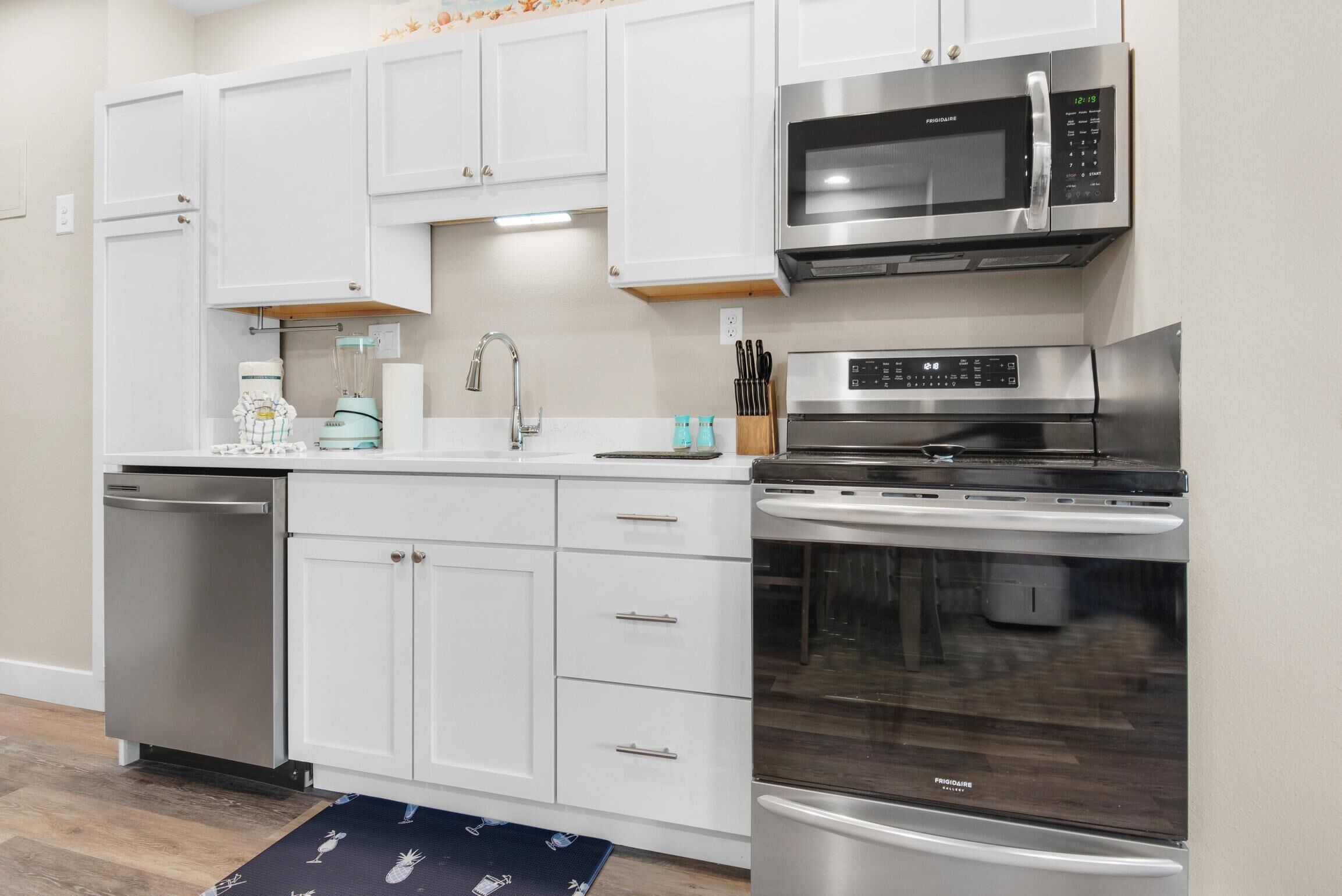 A modern kitchen with white cabinets, a stainless steel dishwasher, a microwave, a stove, and a refrigerator.