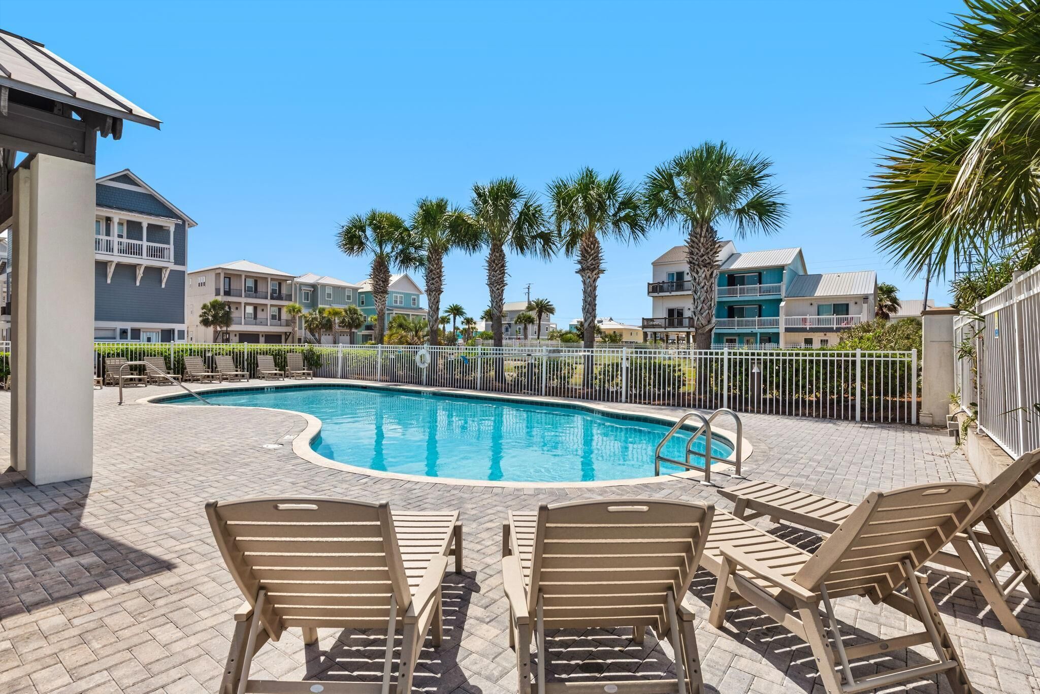 A swimming pool with lounge chairs, palm trees, and multi-story buildings in the background.
