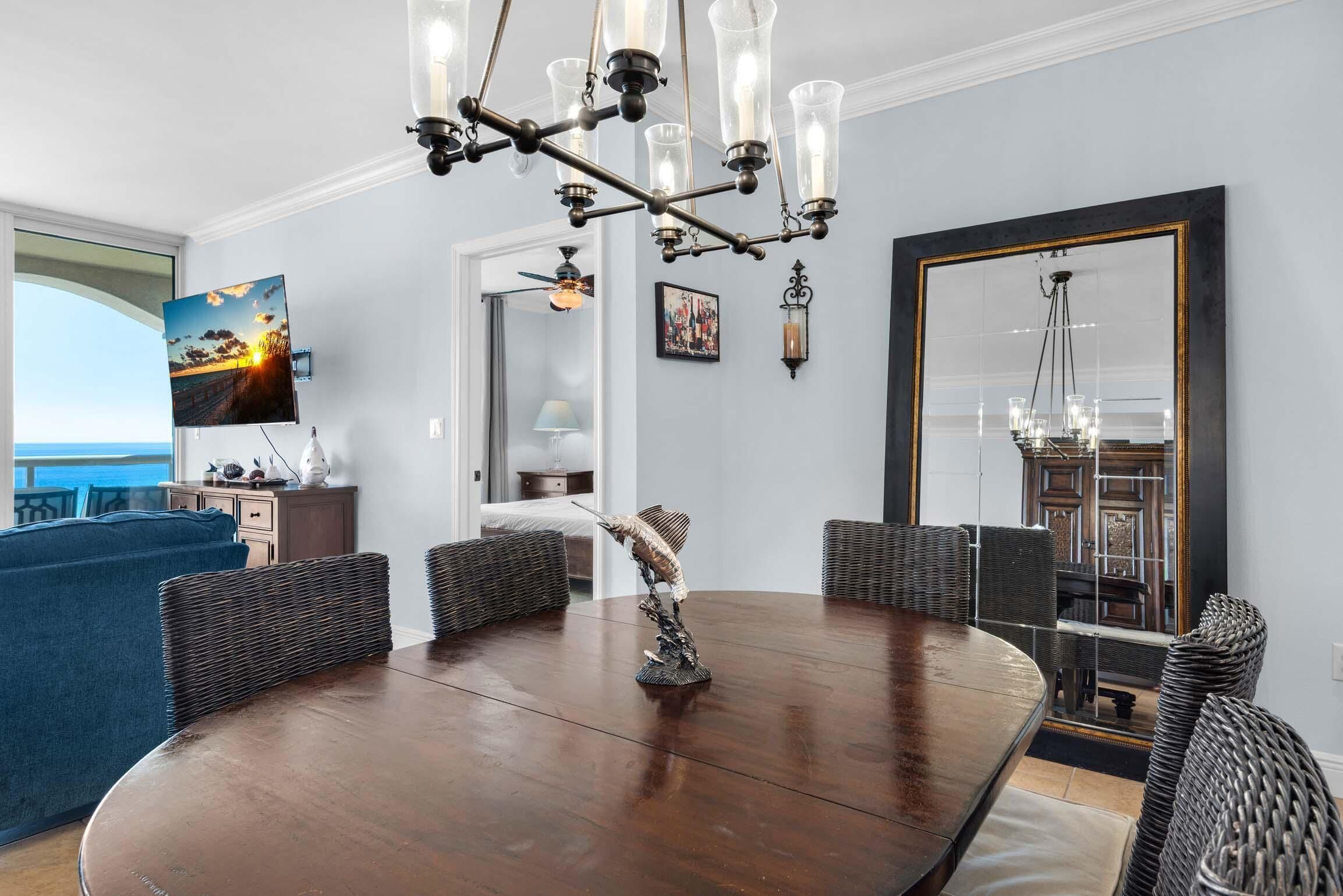 A dining area with a round wooden table, wicker chairs, a decorative bird sculpture, and a chandelier.